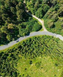 Luftaufnahme der Straße mit Wald und schwarzes Auto | © villacher-alpenstrasse.at/Stabentheiner